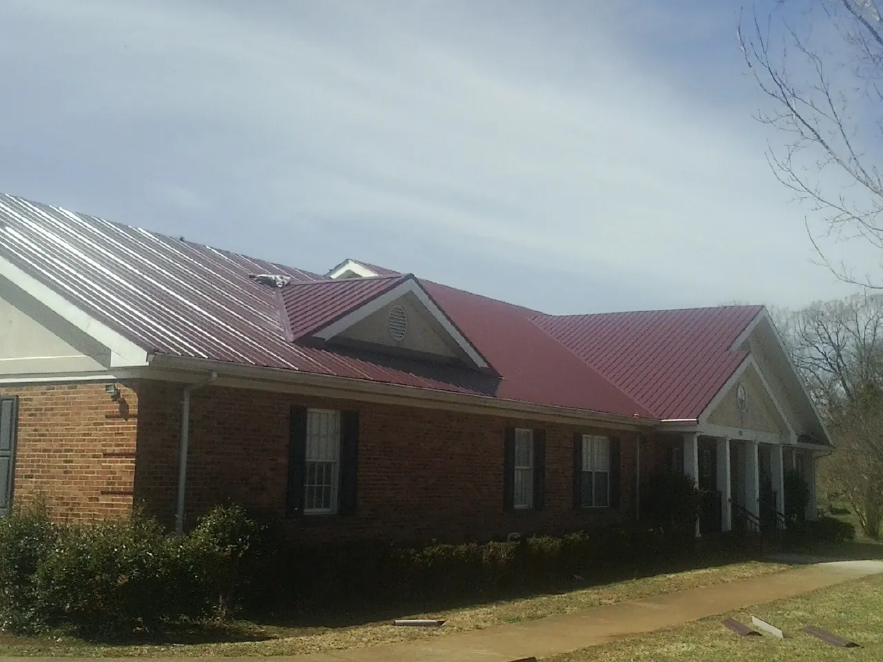 Red metal roof with gabled entries on a long brick building, from a Hail Damage Roof Repair job in Falling Waters