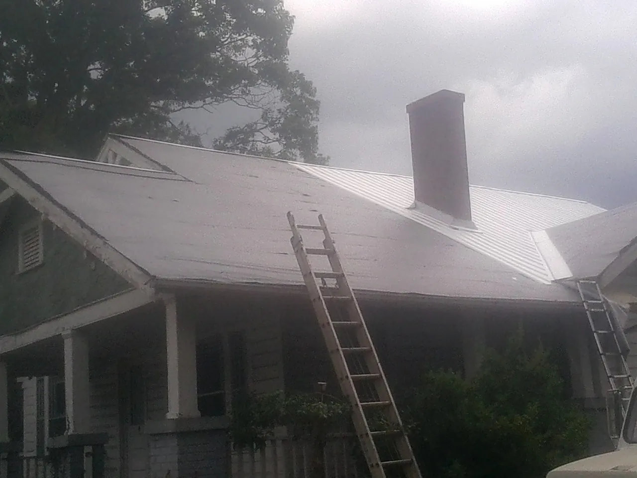 Ladders against a metal roof on an older home with a brick chimney in Falling Waters