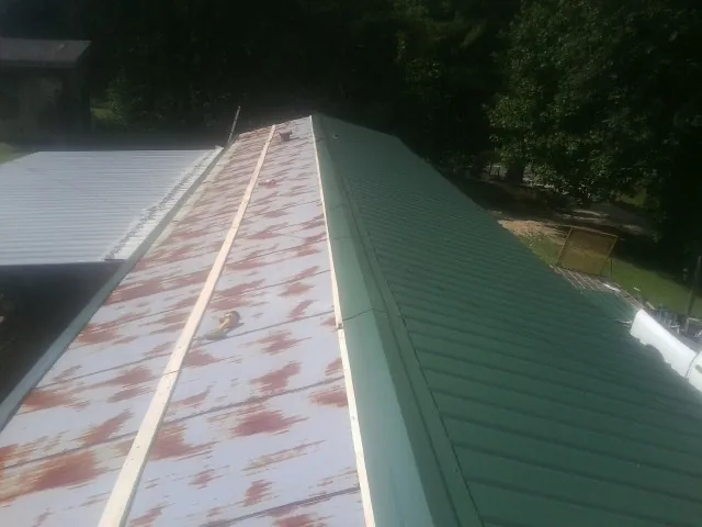 Old rusted panels beside newly installed green metal roofing — Wind Damage Roof Repair by Roofing Brothers in Falling Waters