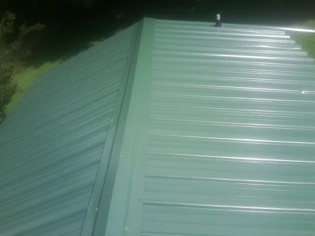 New green metal panels meeting at the ridge of a roof — Flat Roof Repair work by our crew in Falling Waters