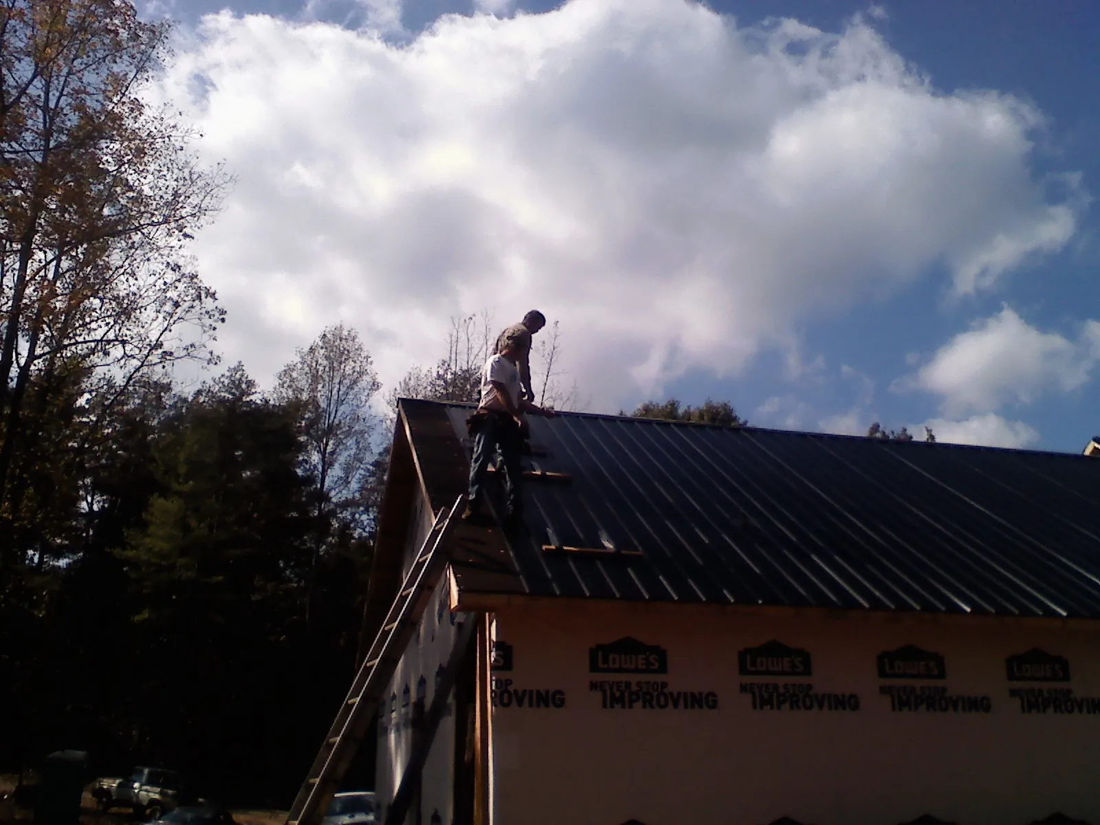 Roofer fastening dark metal panels high against a cloudy sky, from a Roof Inspection job in Falling Waters