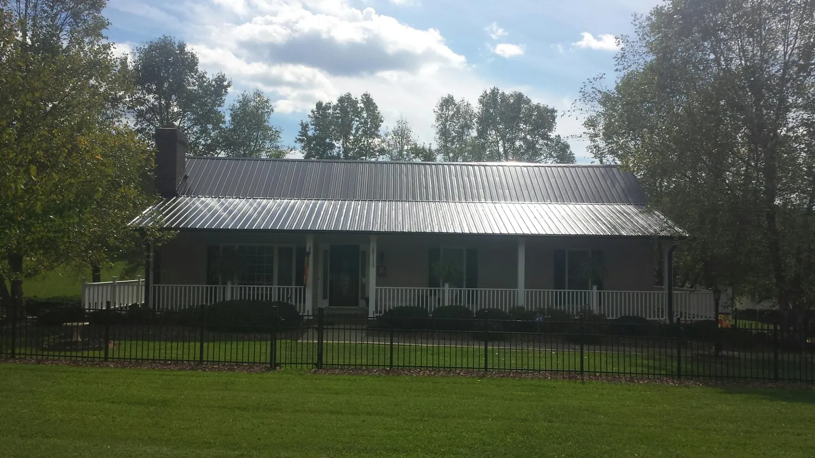 Gray metal roof on a brick ranch with a full width front porch — Gutter Guard Installation work by our crew in Falling Waters