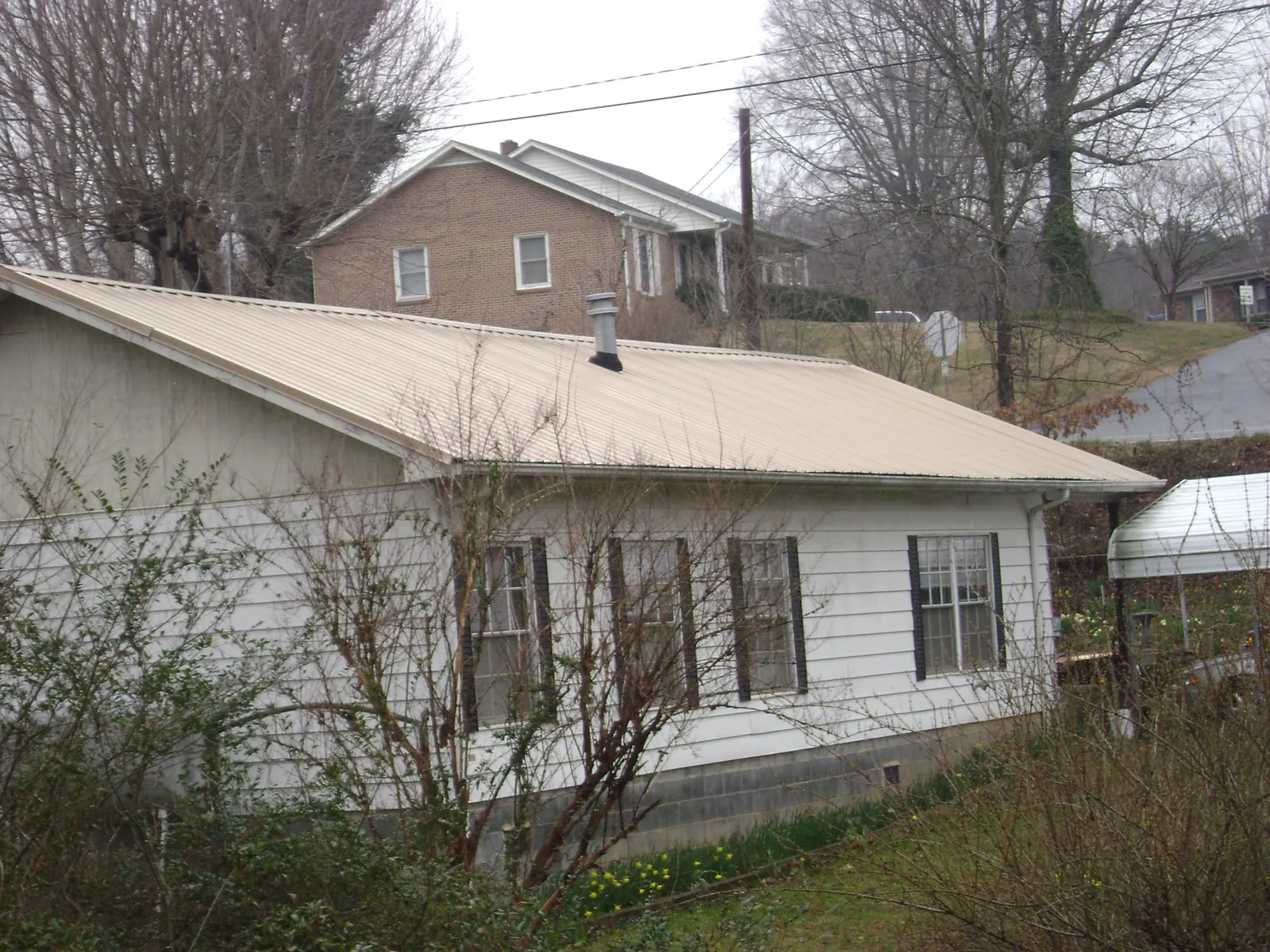 Tan metal roof on a white sided house set into a hillside — Commercial Roofing by Roofing Brothers in Falling Waters